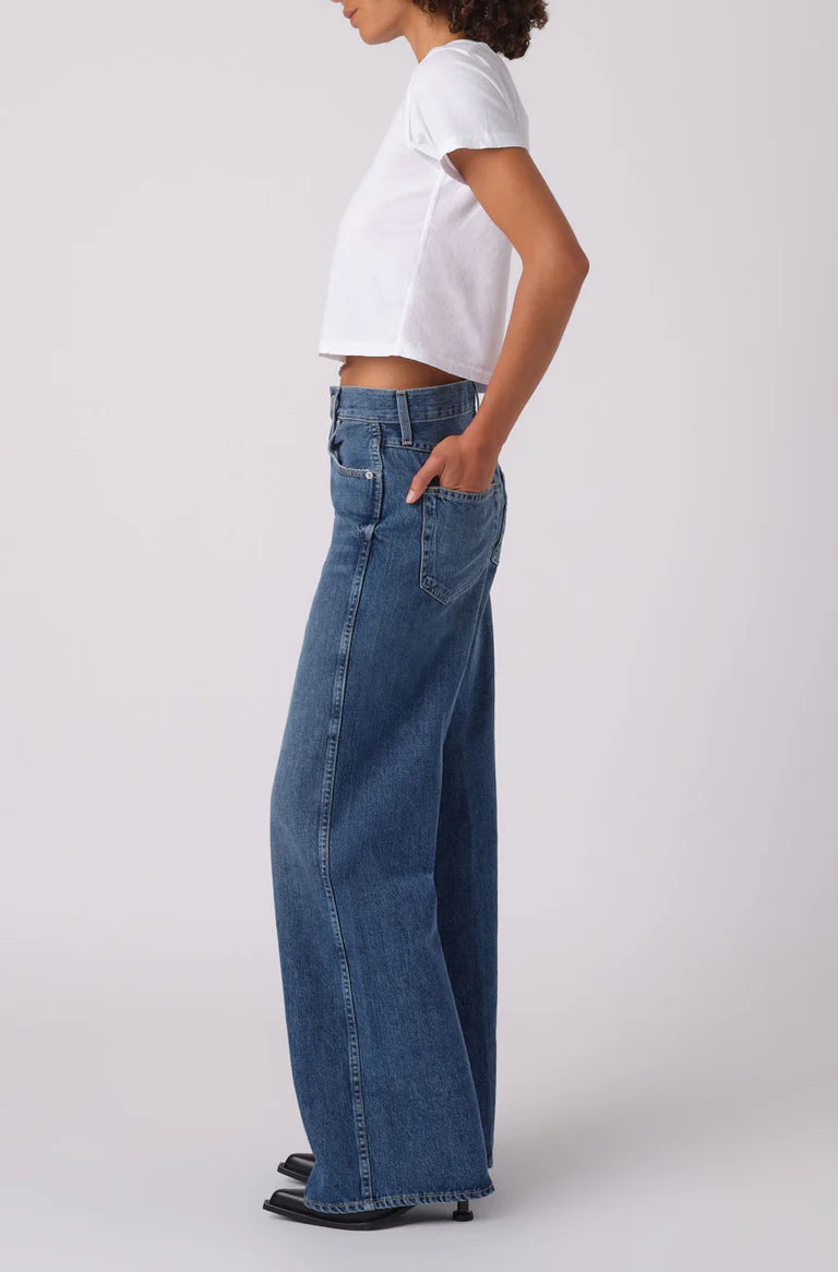 Person wearing blue wide-leg jeans and a white top on a white background