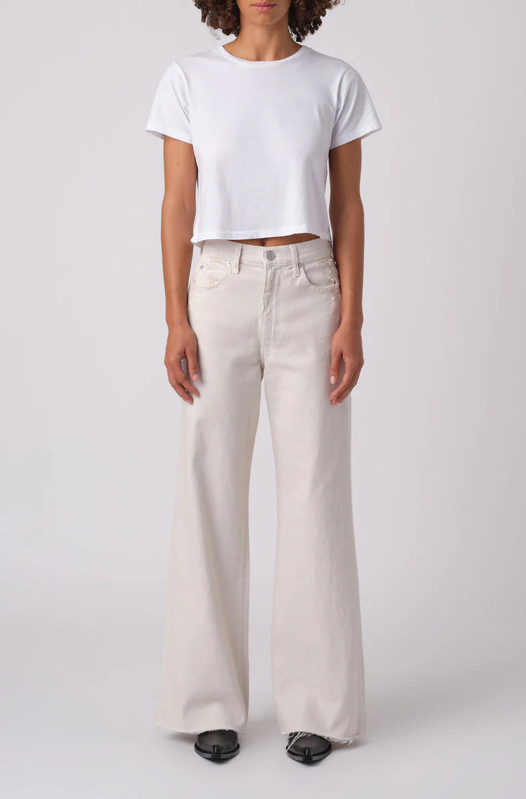 Person wearing a white t-shirt and light-colored wide-leg jeans on a plain background