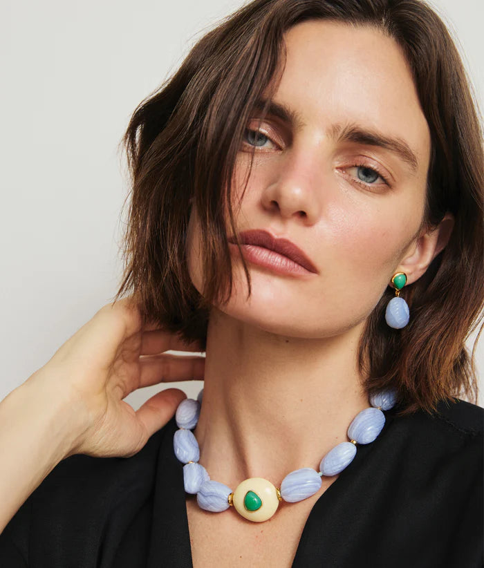 Woman wearing a necklace with a green and gold pendant and blue beads.