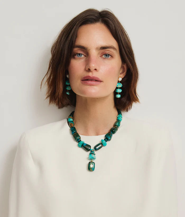 Woman wearing a green beaded necklace and earrings against a plain background