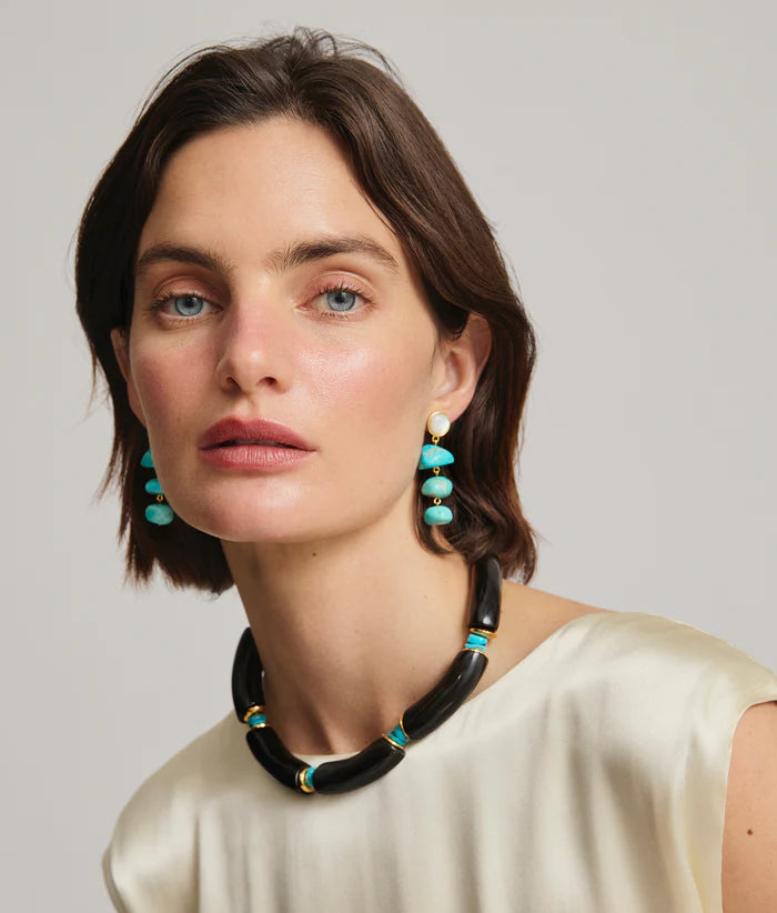 Woman wearing a black and turquoise beaded necklace and earrings against a neutral background