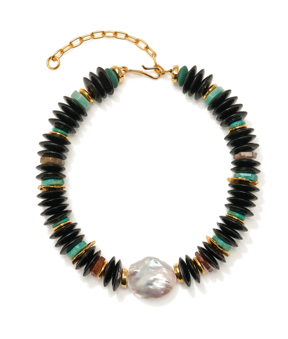 A beaded necklace featuring black disc-shaped beads, small turquoise green beads, gold spacer rings, and a large irregular white pearl at the bottom center, displayed on a clean white background.