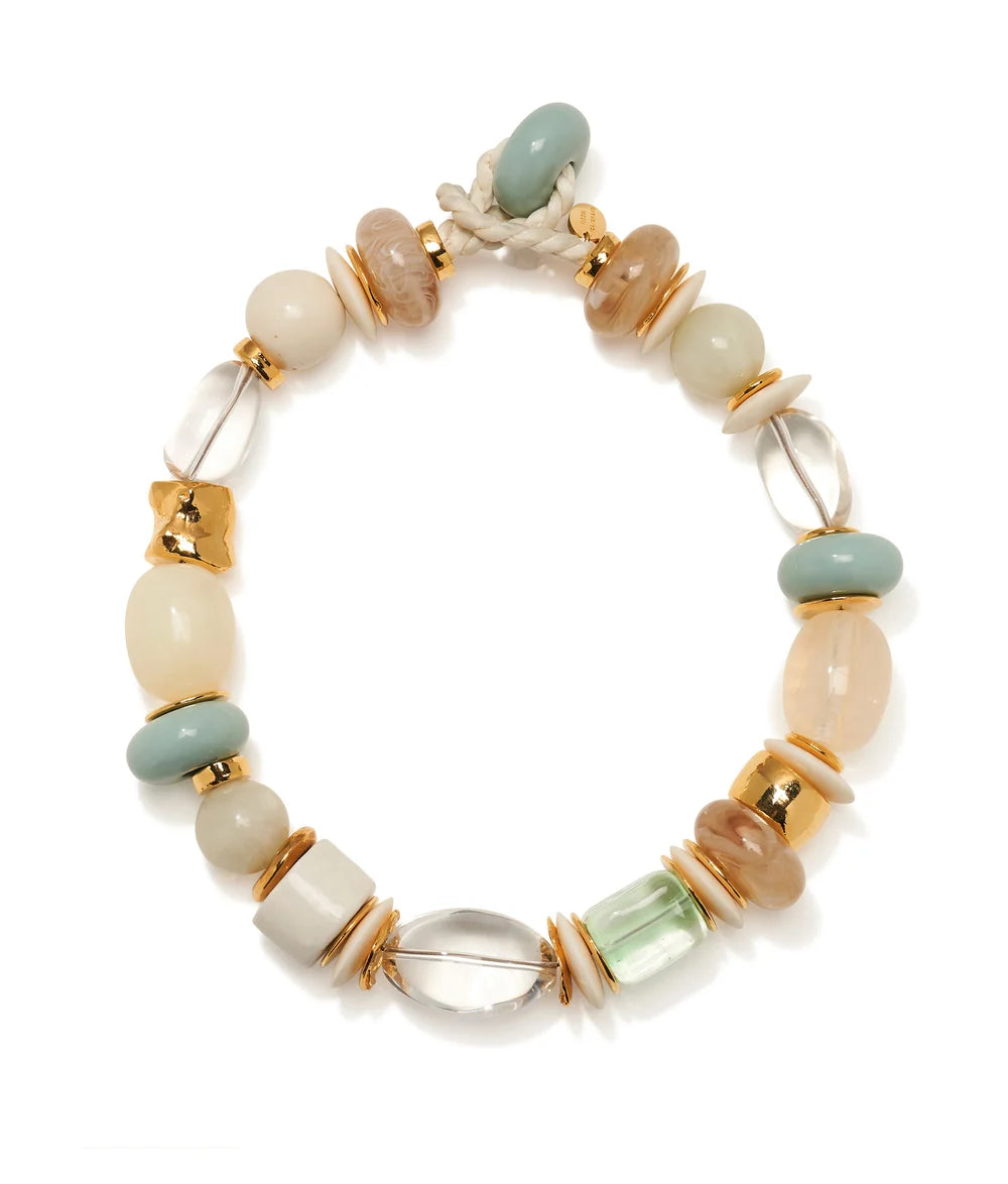 A beaded stretch bracelet featuring a mix of matte cream, sage green, light brown, and clear glass beads, accented with gold-toned spacers and a white rope clasp, shown on a white background.