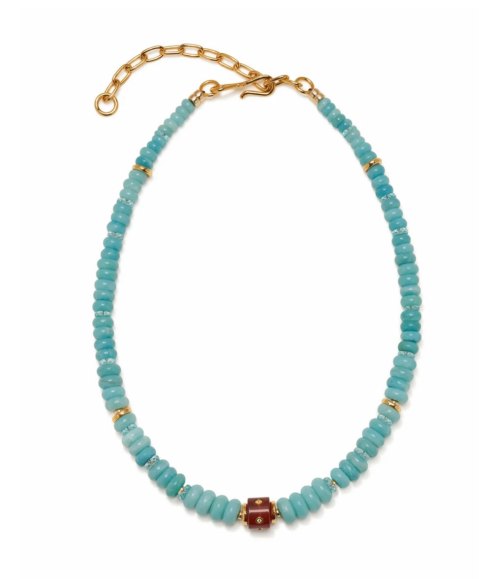 A beaded necklace featuring light blue turquoise-like round beads, accented with small gold spacer beads and a central reddish-brown rectangular bead, finished with a gold chain extender and lobster clasp on a white background.