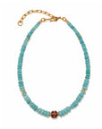 A beaded necklace featuring light blue turquoise-like round beads, accented with small gold spacer beads and a central reddish-brown rectangular bead, finished with a gold chain extender and lobster clasp on a white background.