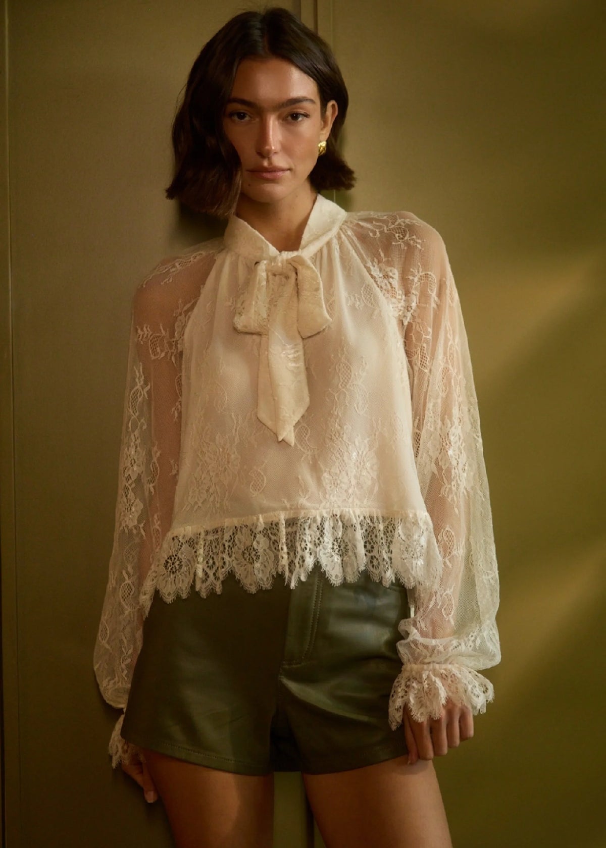model wearing a lace tie neck long sleeve top with shorts on a green backround