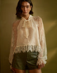 model wearing a lace tie neck long sleeve top with shorts on a green backround
