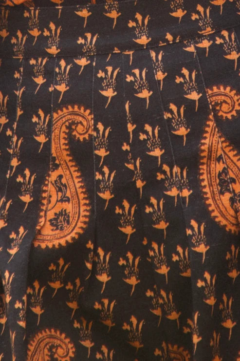 A close-up of a dark fabric with an orange paisley and floral block print pattern.
