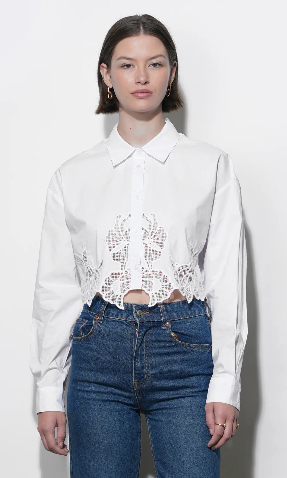 Woman wearing a white blouse with lace detailing and blue jeans on a white background