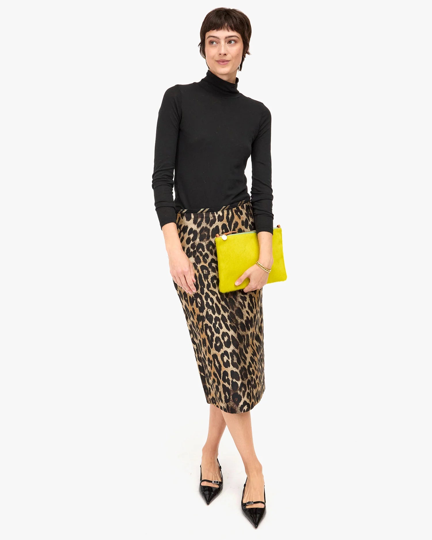 Woman wearing a black turtleneck, leopard print skirt, and yellow clutch on a white background