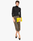 Woman wearing a black turtleneck, leopard print skirt, and yellow clutch on a white background