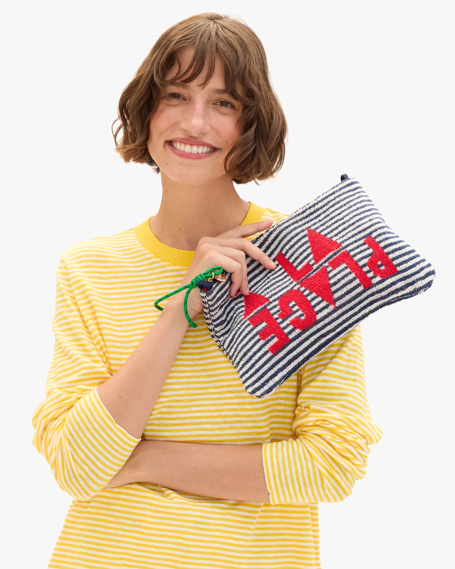 Woman holding a striped pouch with 'PLAGE' text, wearing a yellow striped shirt.