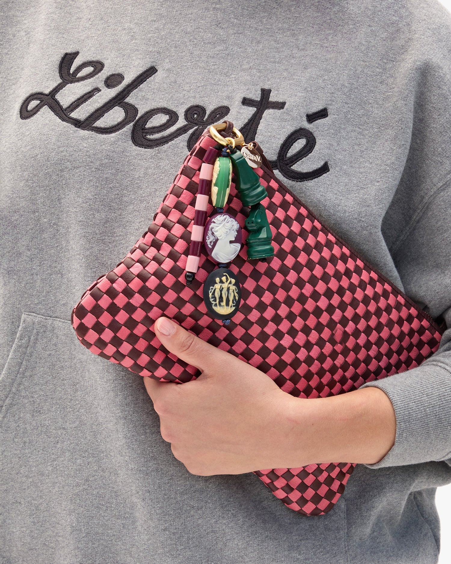 Person holding a pink checkered clutch with Cameo Fob against a gray sweatshirt background.