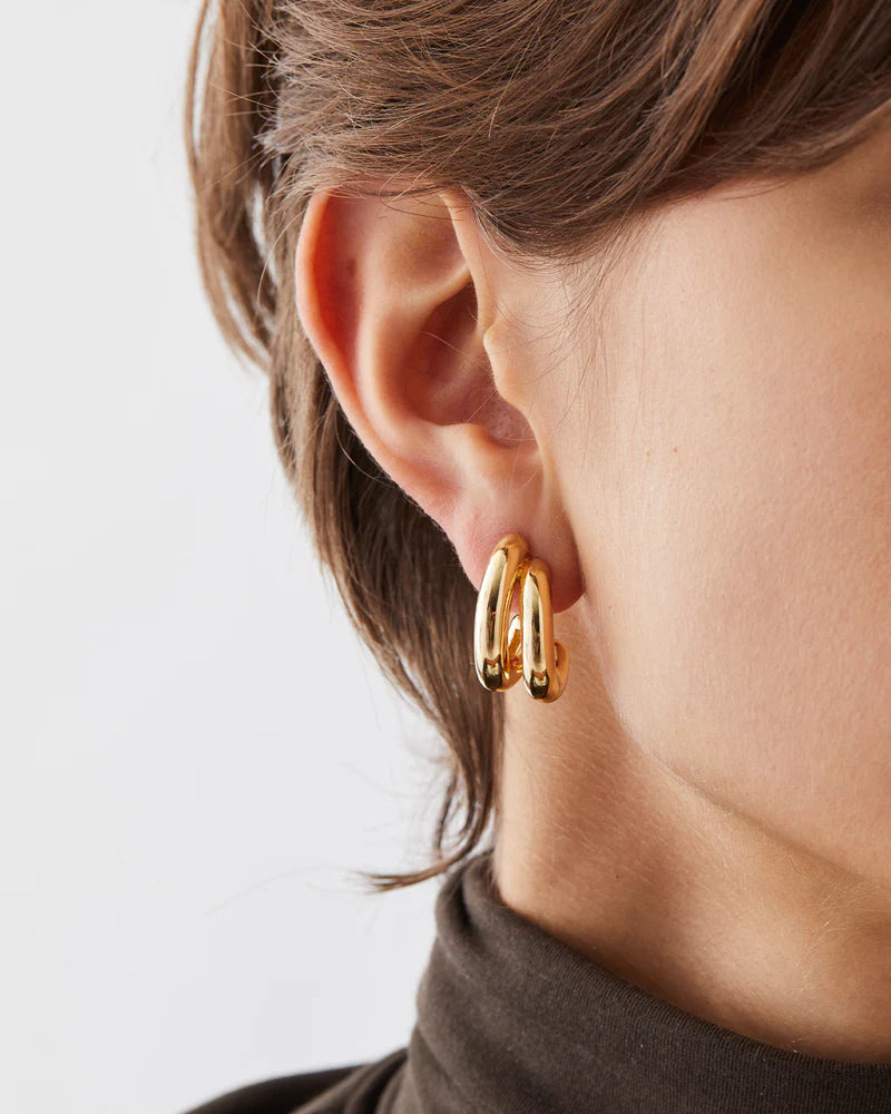 Gold hoop earrings worn by a person with a neutral background