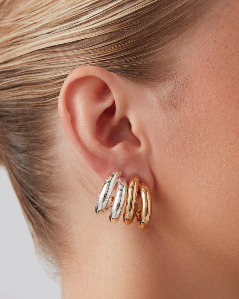 Close-up of an ear wearing a gold and silver hoop earring on a neutral background