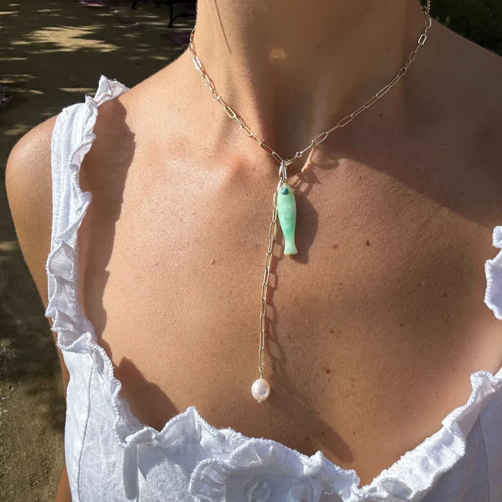 Necklace with a green pendant and pearl drop worn by a person in a white top.