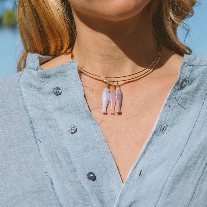 Close-up of a person wearing a necklace with fish-shaped pendants against a blurred outdoor background.