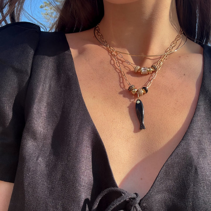 Close-up of a person wearing a layered gold necklaces with a fish pendant.