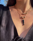 Close-up of a person wearing a layered gold necklaces with a fish pendant.
