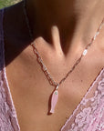 Necklace with a pink pendant worn by a person in a pink lace top.
