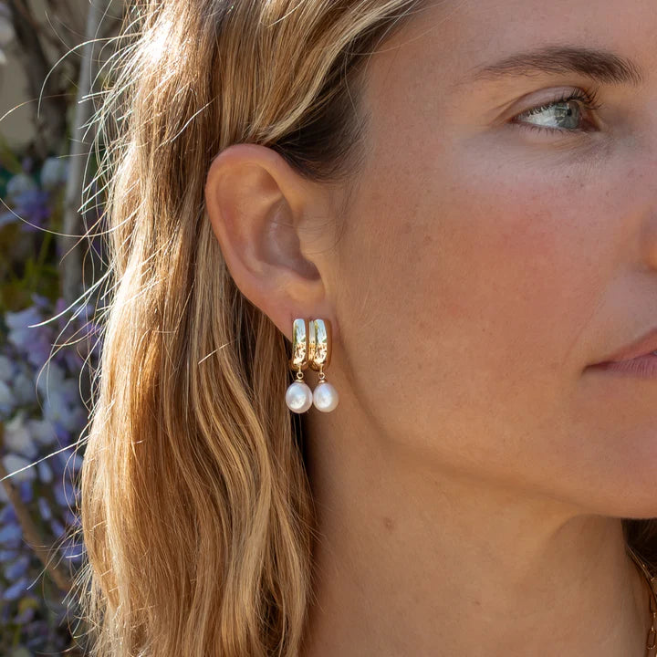 Close-up of a woman wearing pearl earrings with a blurred natural background