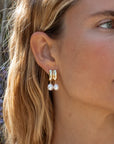 Close-up of a woman wearing pearl earrings with a blurred natural background