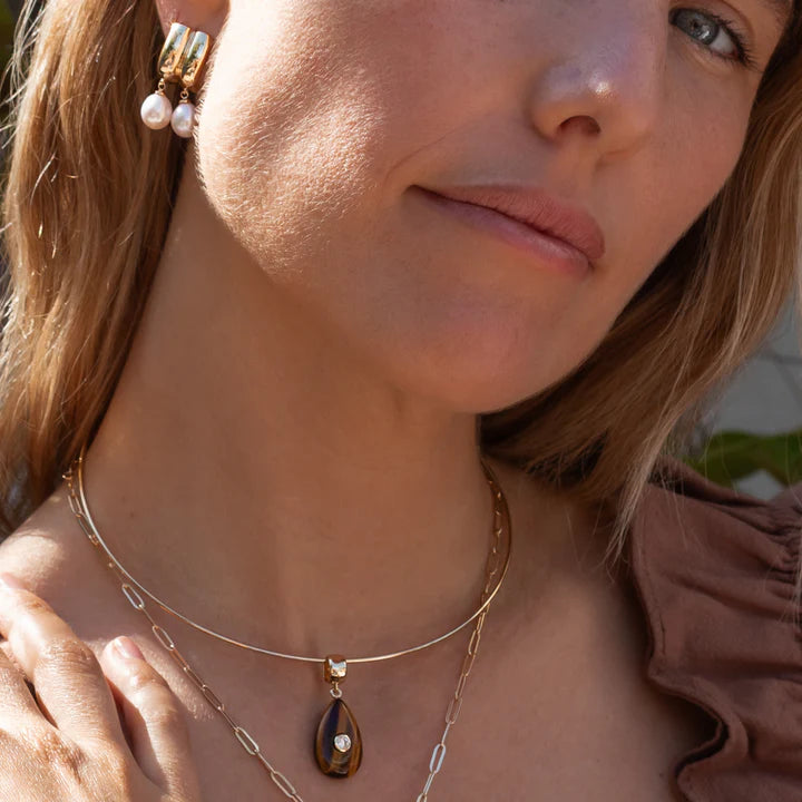 Close-up of a woman wearing a gold necklace with a pendant and pearl earrings.
