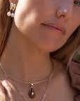 Close-up of a woman wearing a gold necklace with a pendant and pearl earrings.