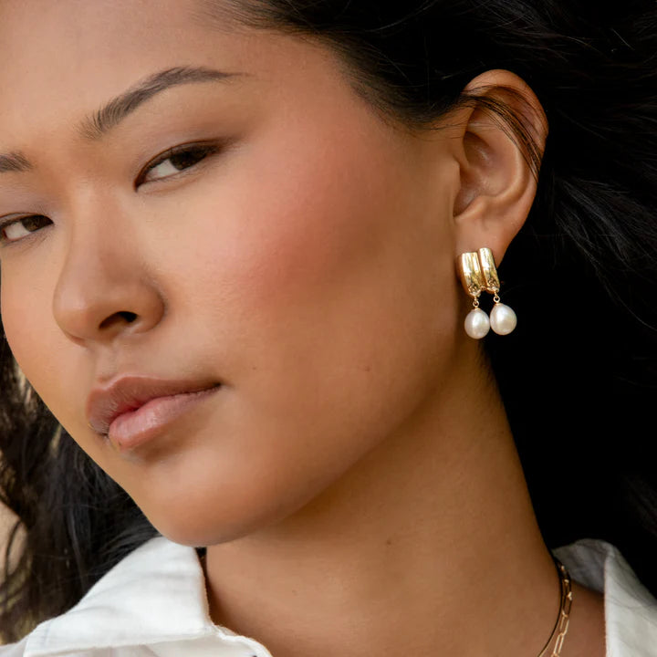 Close-up of a woman wearing gold hoop earrings with pearls.