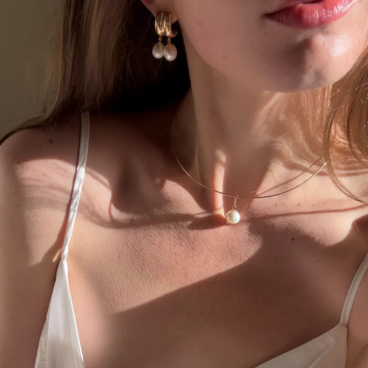 Close-up of a woman wearing pearl earrings and a necklace with a neutral background