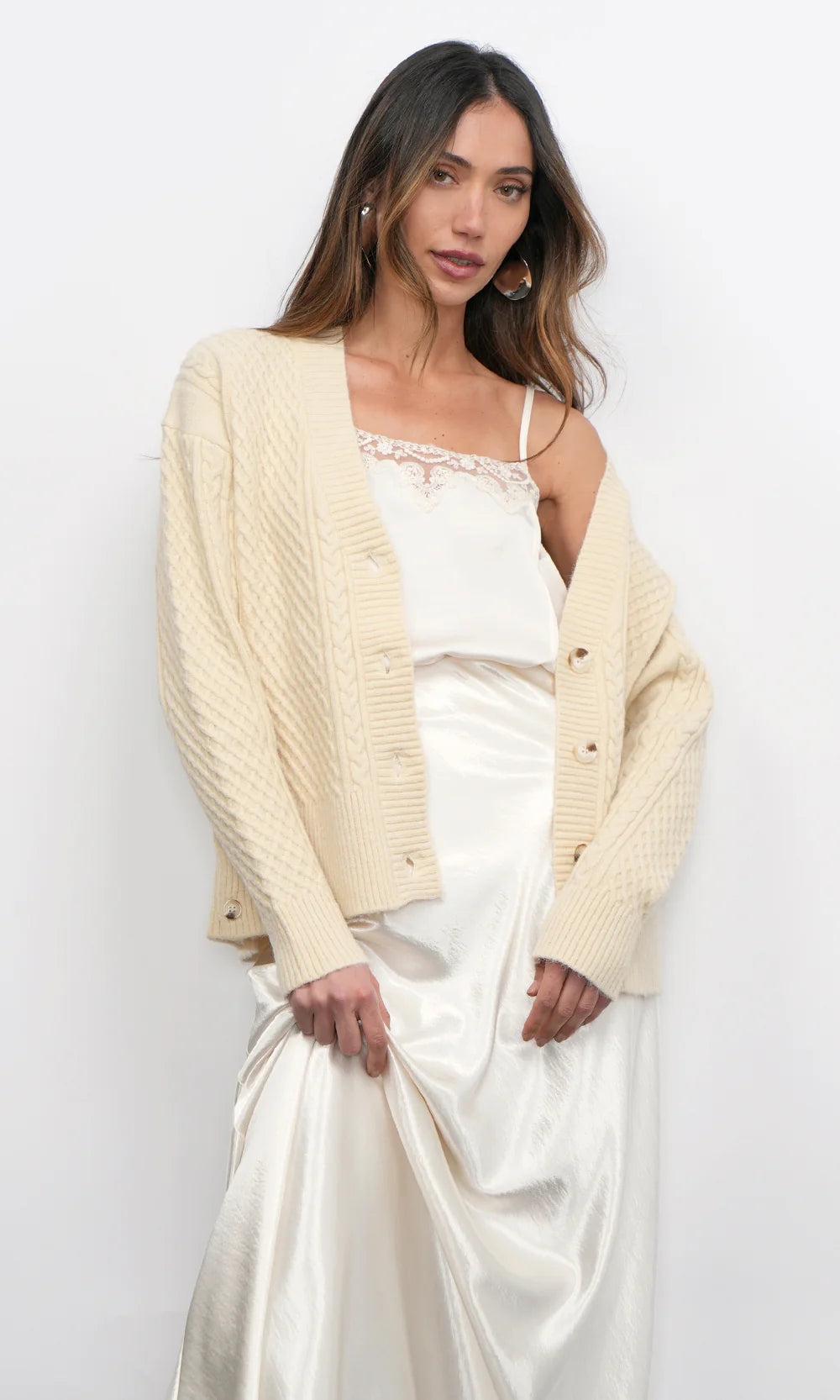 Woman wearing a cream cardigan over a white outfit against a plain background