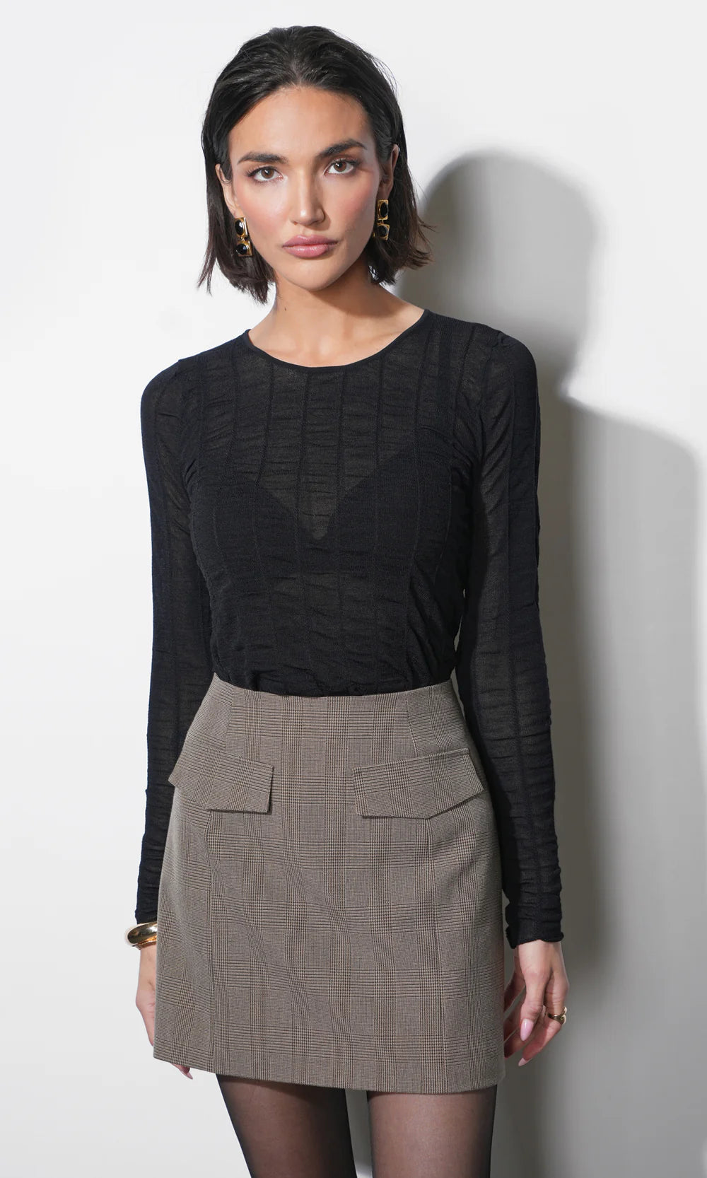 Woman wearing a black long-sleeve top and gray skirt against a white background