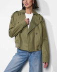 Woman wearing an olive green jacket and blue jeans against a white background, front