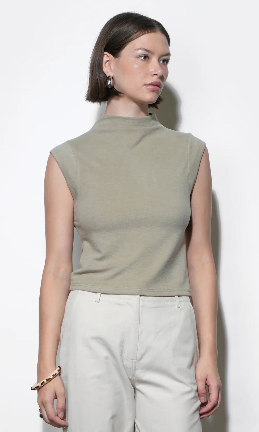 Woman wearing a sleeveless green top and light gray pants against a white background