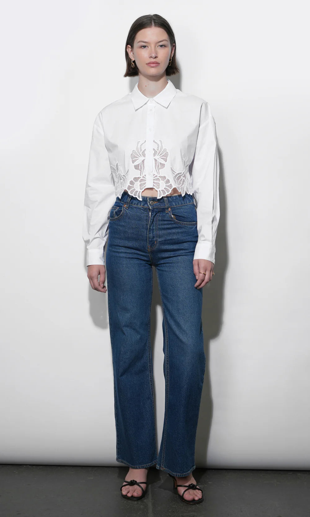 Person wearing a white blouse with lace details and blue jeans against a plain background