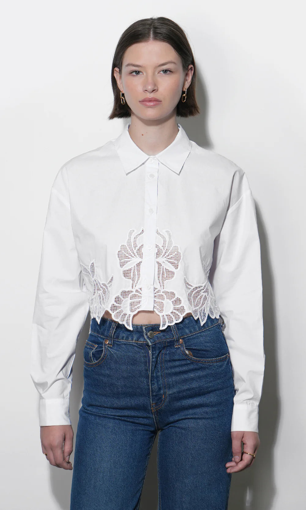 Woman wearing a white blouse with lace details and blue jeans on a white background