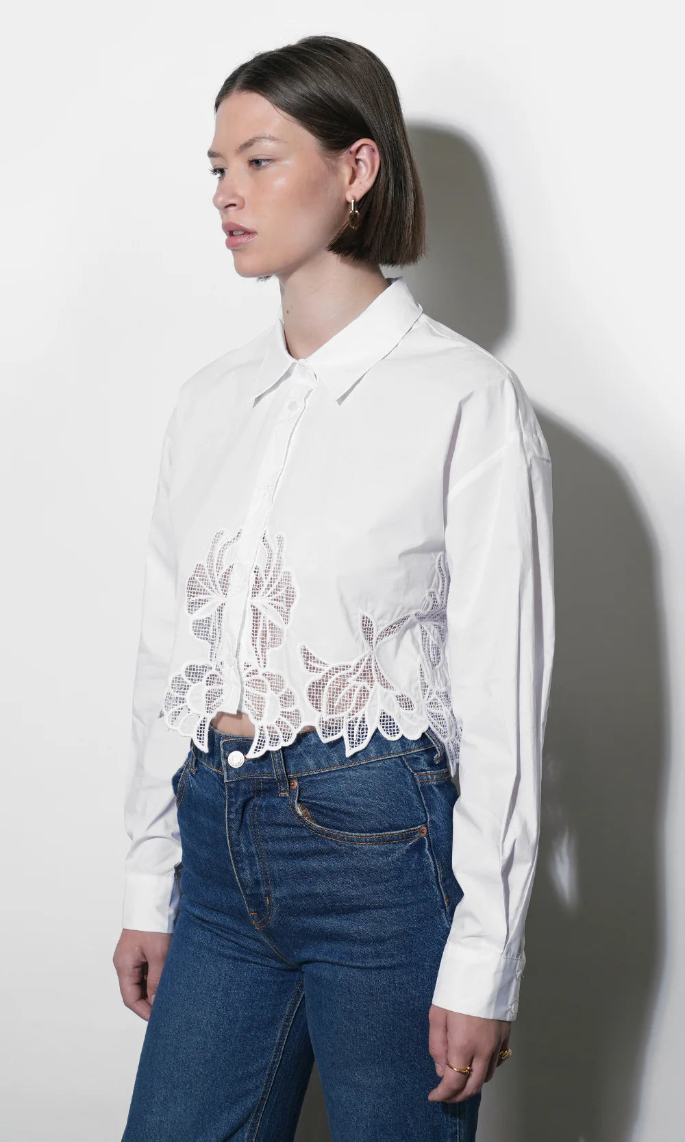 Woman wearing a white blouse with lace details and blue jeans against a white background