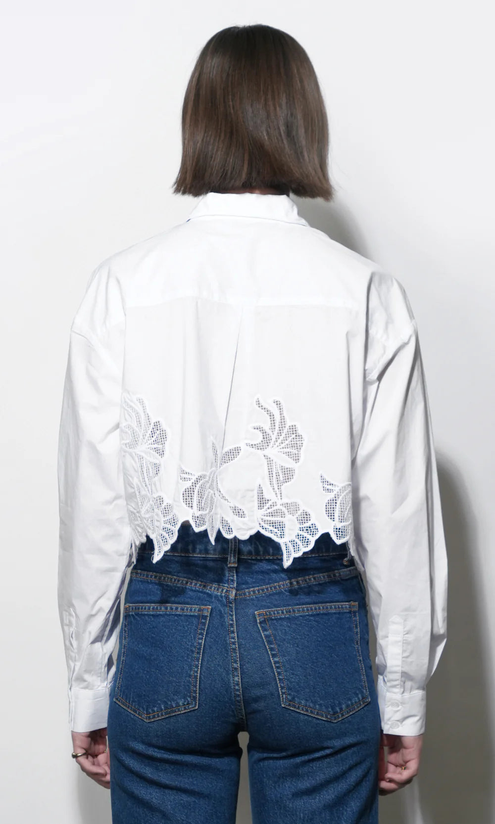 Person wearing a white blouse with lace details and blue jeans on a plain background