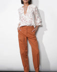 Woman wearing a white floral blouse and orange pants against a white background