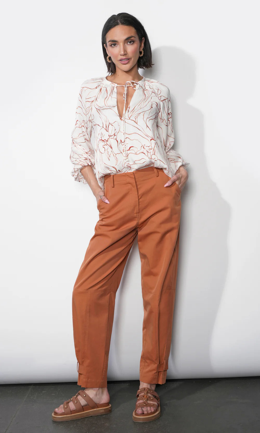 Woman wearing a white blouse with lace details and brown pants against a white background