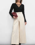 Woman wearing a black top and beige wide-leg pants holding a red clutch against a white background, full body