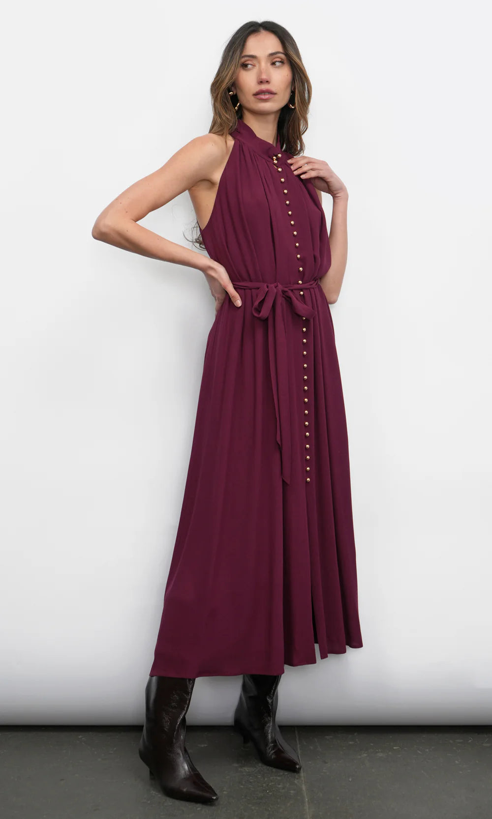 Woman wearing a burgundy dress with button details against a white background, front/side view