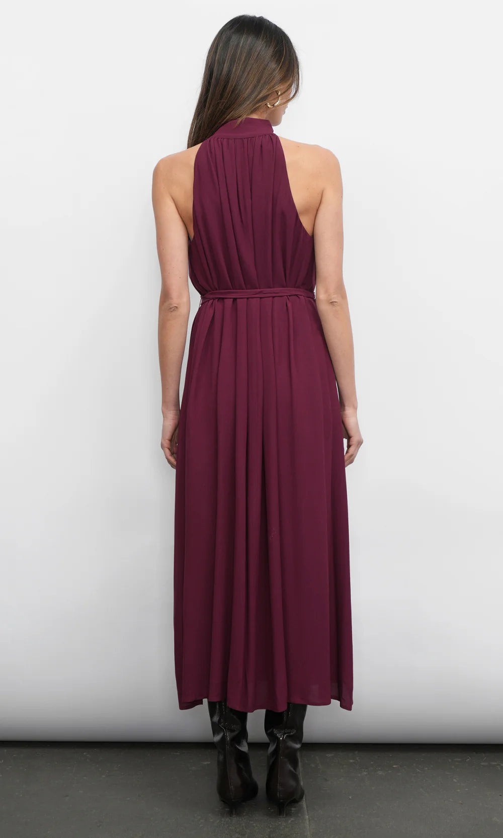 Woman wearing a burgundy halter neck dress against a white background, back view
