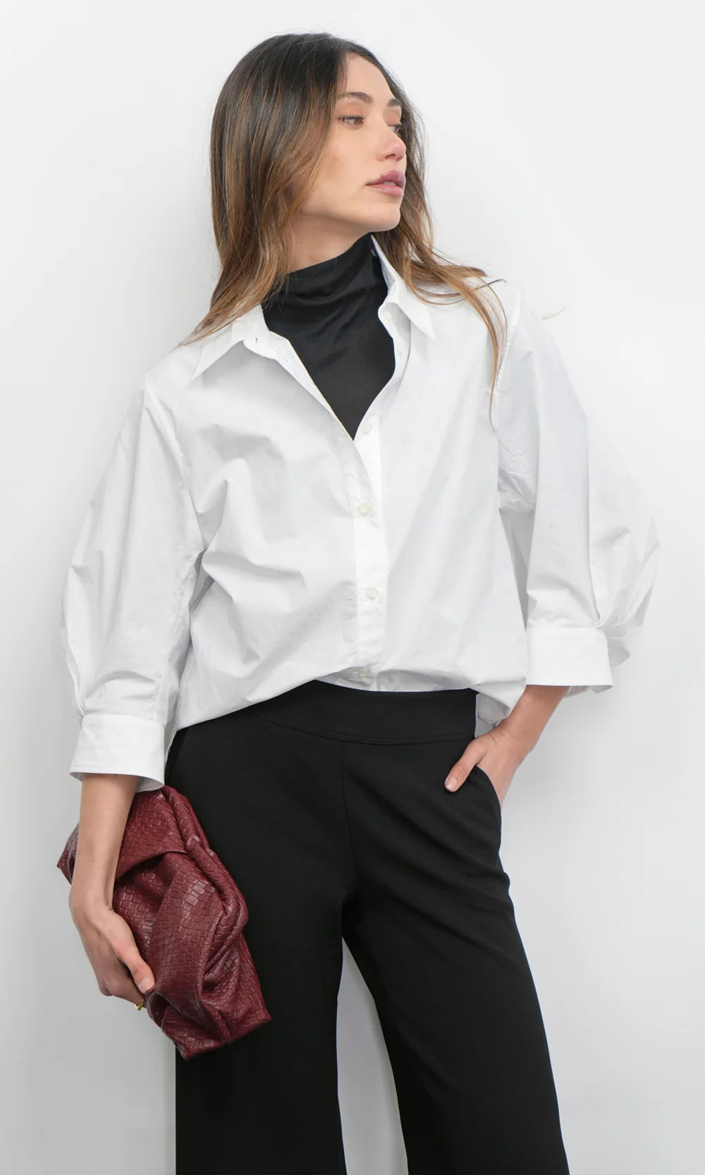 Woman wearing a white shirt over a black turtleneck with black pants against a white background