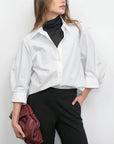 Woman wearing a white shirt over a black turtleneck with black pants against a white background