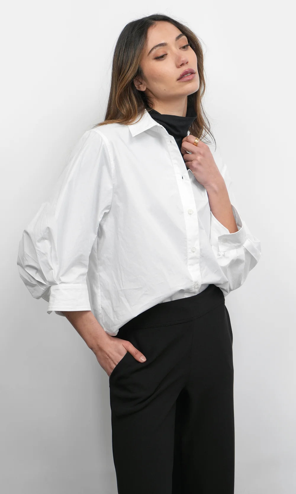 Woman wearing a white shirt and black pants against a plain background