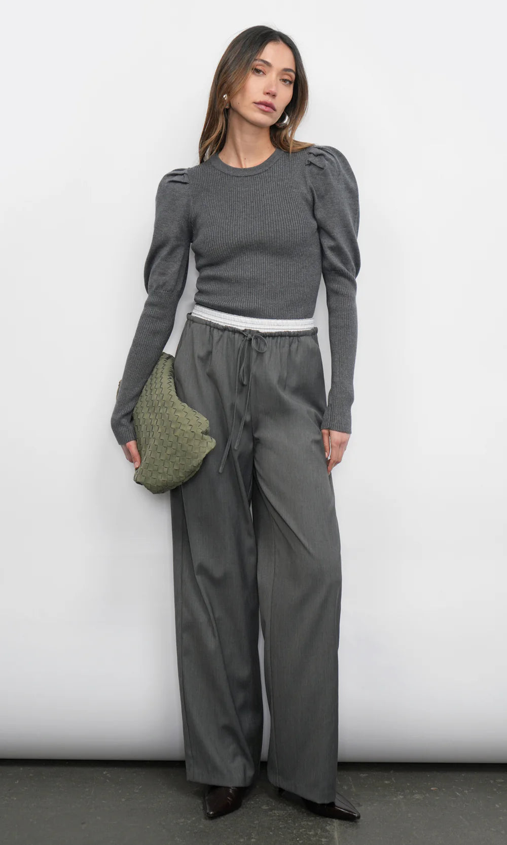 Woman wearing a gray outfit with wide-leg pants and a green bag against a white background