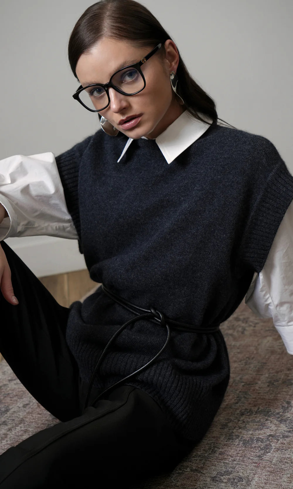 Woman wearing a dark sweater vest over a white shirt with a plain background