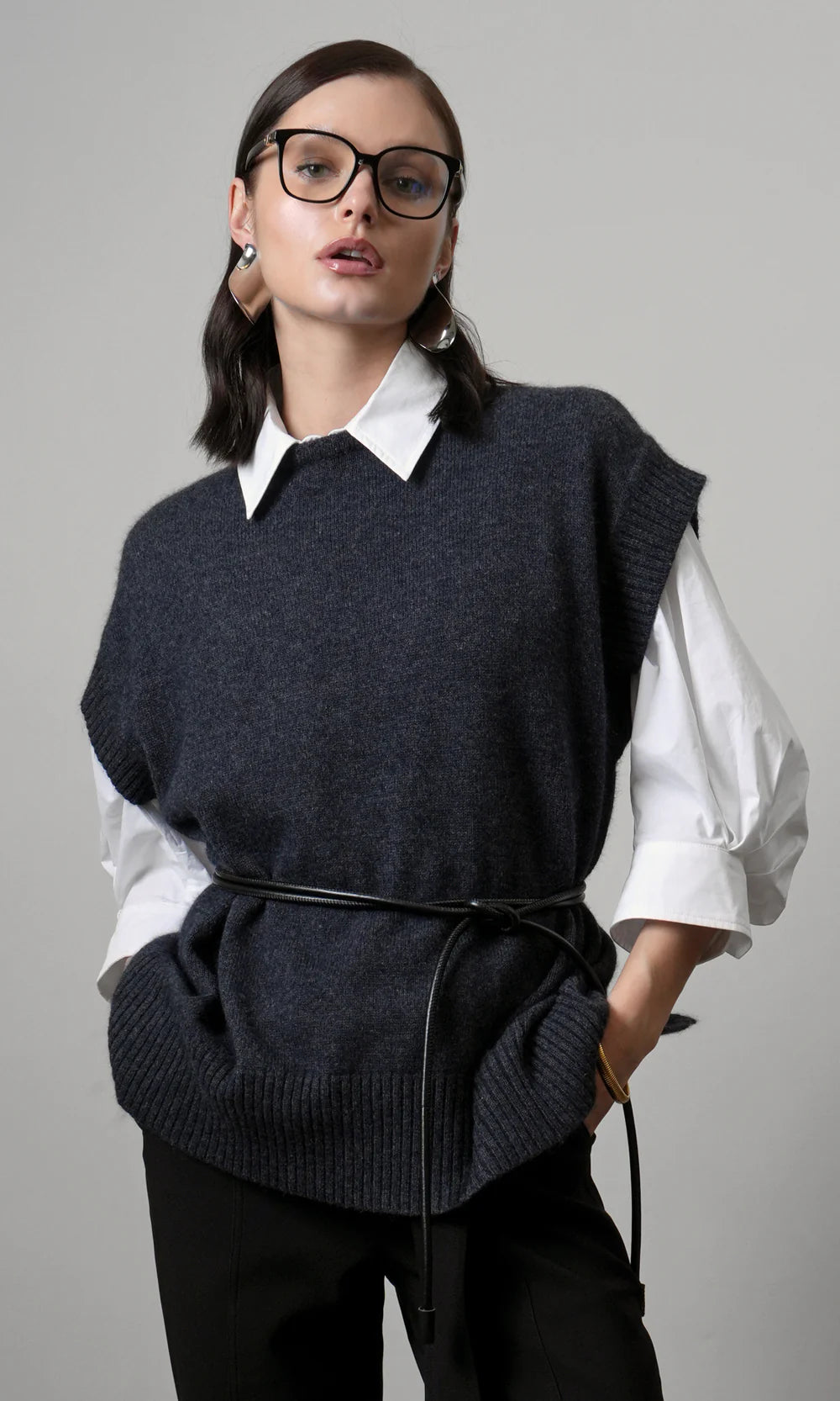Woman wearing a dark gray sweater vest over a white shirt on a gray background