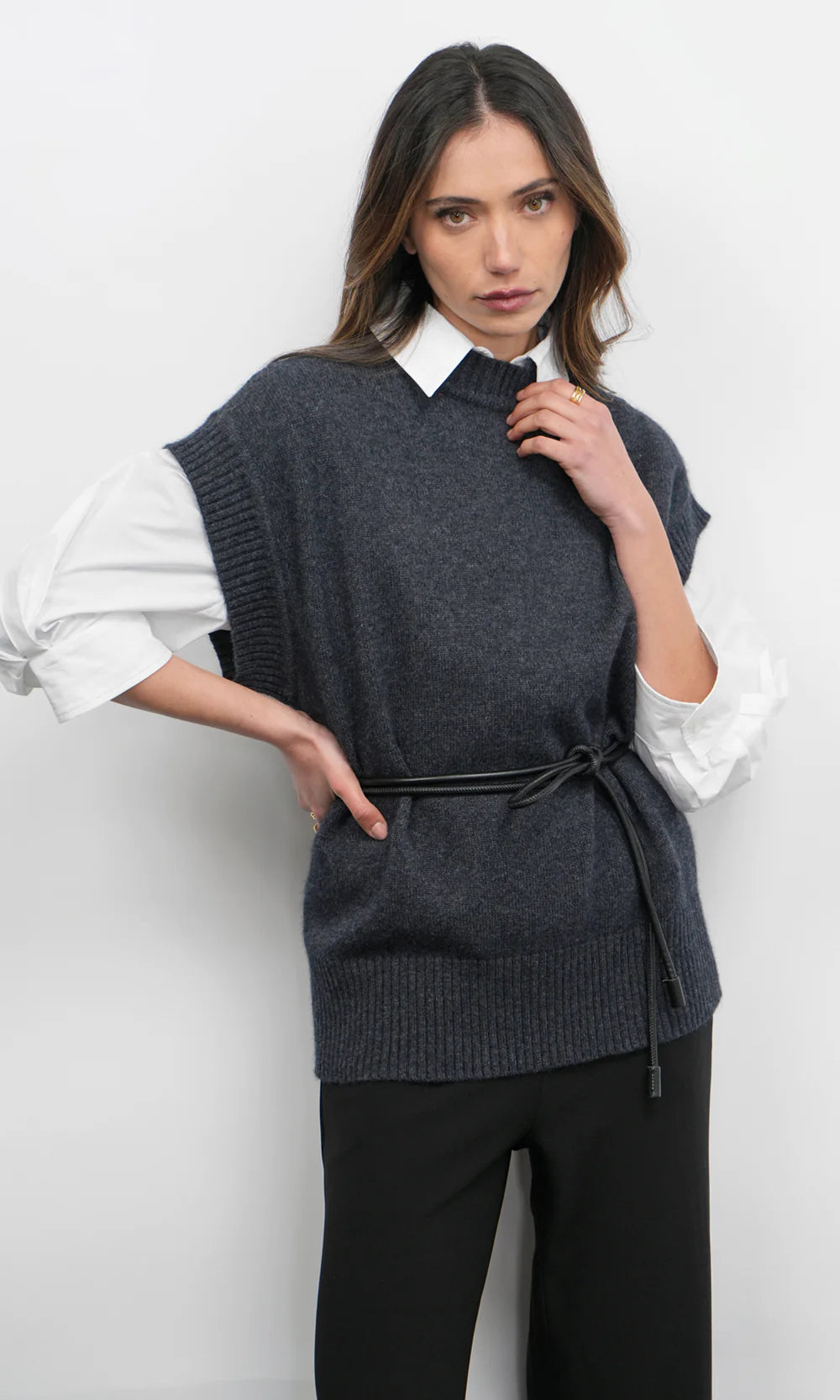 Woman wearing a dark gray knitted vest over a white shirt with a plain background, front view
